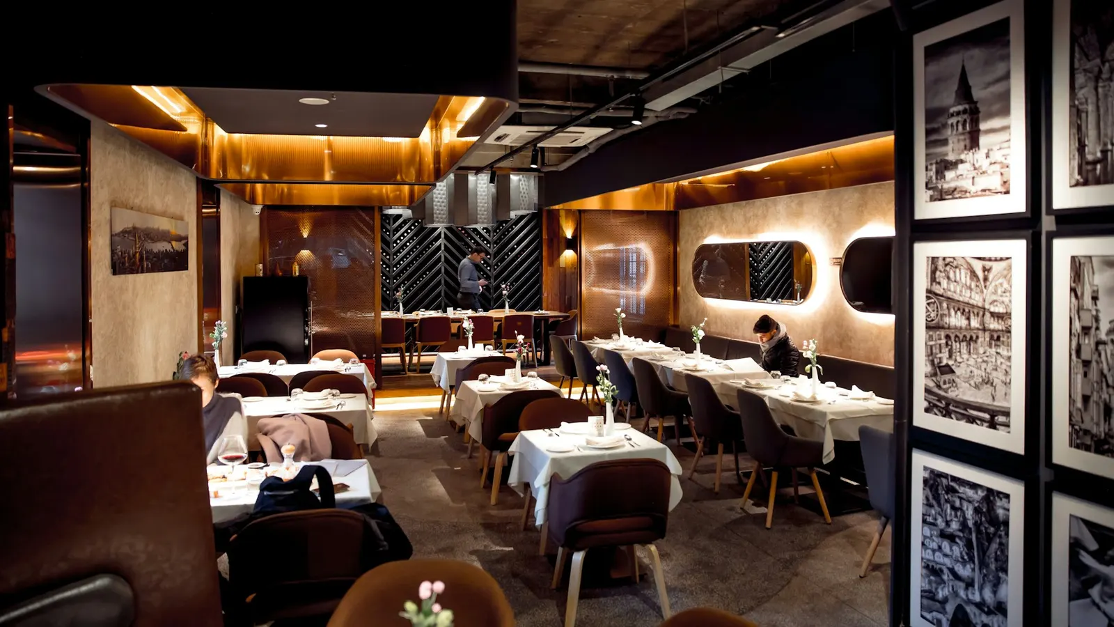 Warmly lit dining room with upholstered booths and tables set for dinner